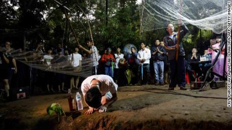 Family members and relatives pray at the entrance of Tham Luang cave while rescue personnel conduct operations to find their children.