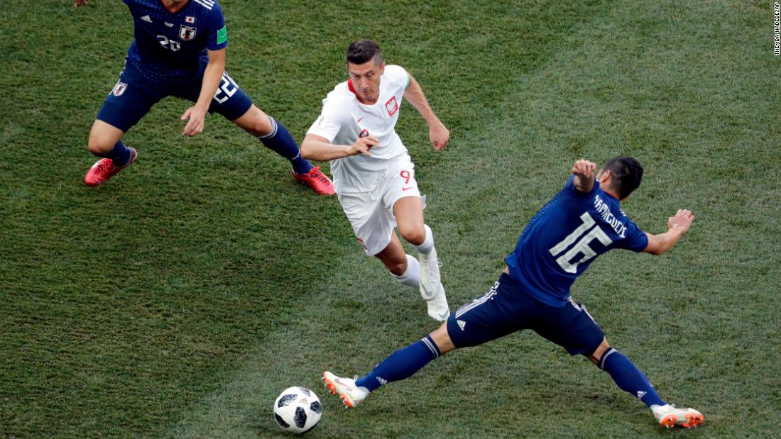 Poland forward Robert Lewandowski dribbles through two Japan players.