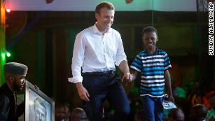 French President Emmanuel Macron, left, walks on stage at the New Africa Shrine in Lagos with 11-year-old, Kareem Waris Olamilekan, a young Nigerian artist who drew his portrait. 