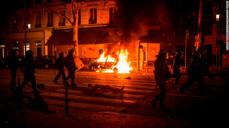 French anti-riot police officers walk by a burning car during clashes in Lyon on Sunday night. 