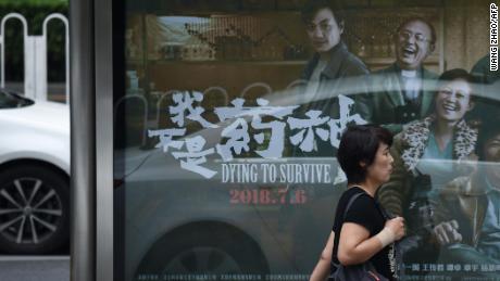 A woman walks past a poster of the film &quot;Dying to Survive&quot; at a bus stop in Beijing on July 12.
