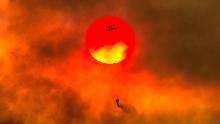 In this Friday, July 27, 2018 photo, a firefighting helicopter makes a water drop as the sun sets over a ridge burning near Redding, Calif., in efforts against the Carr Fire. Scorching heat, winds and dry conditions complicated firefighting efforts. (Hector Amezcua/The Sacramento Bee/ AP