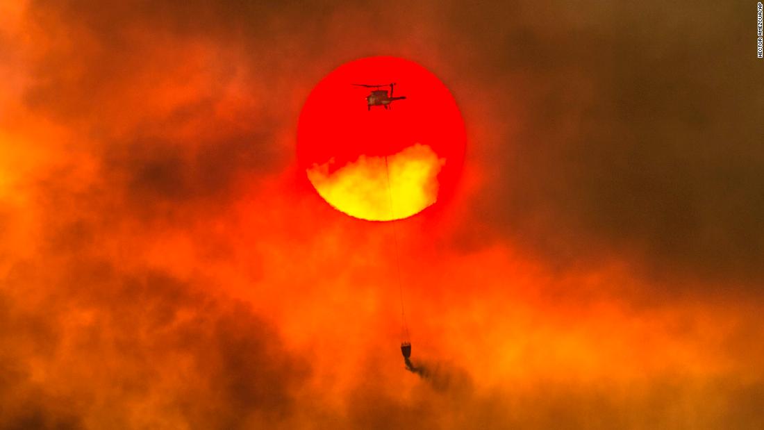 A firefighting helicopter makes a water drop as the sun sets over a ridge burning near Redding on July 27.