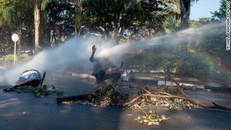 A protester is hit in the face with a water cannon outside the gates of the ZImbabwe Electoral Commission during a protest against polling results in Harare.