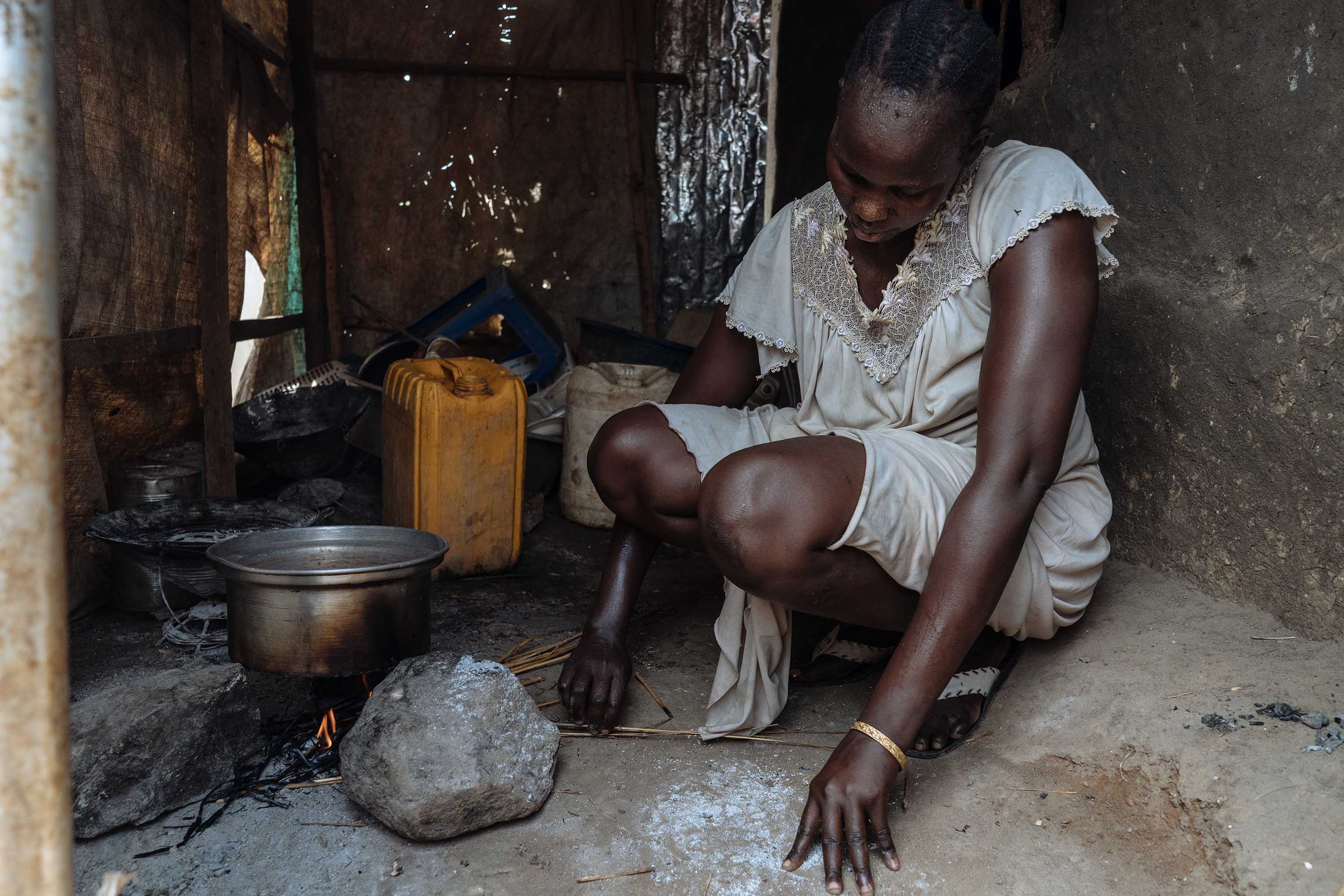 Angeline, a South Sudanese woman, photographed making a fire in her kitchen. 