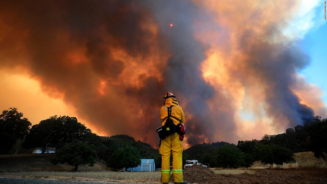 A tower of smoke pours from Cow Mountain as a firefighter keeps a watch on surrounding vegetation.