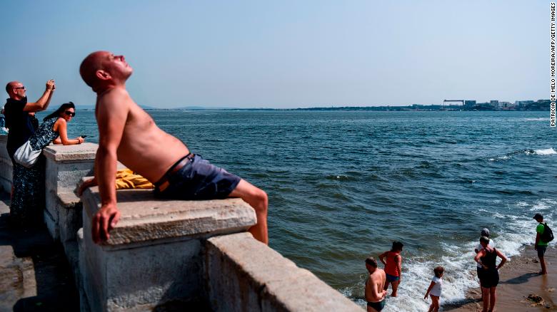 A man sunbathes Friday as others cool off in the Tagus River in Portugal's capital, Lisbon.