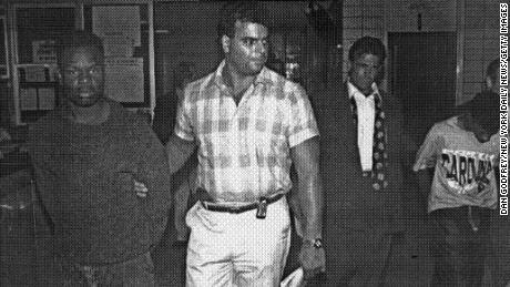 John Bunn, 14, right, and Rosean Hargrove, 17, arrested at the 77th Precinct in Brooklyn in August 1991. NYPD Detective Louis Scarcella (open jacket and loose tie) holds Bunn.