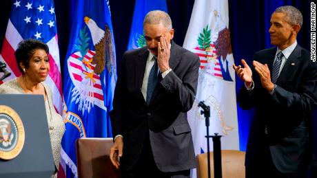 Um Procurador-Geral Eric Holder, centro, e o Presidente Barack Obama reagem após Franklin ter terminado de cantar uma canção para Holder num evento que celebrava o fim do seu mandato no Departamento de Justiça em 2015.