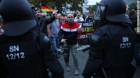 A right-wing supporter gestures to journalists Monday as riot police stand by during a confrontation with leftists the day after a man was fatally stabbed.