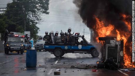Heavily armed police officers sit on a pick-up and stand next to a burning police car in Managua on September 2, 2018.