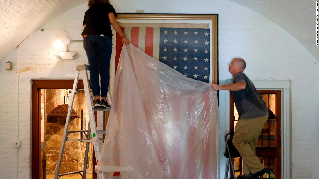 Veronica Gallardo and Robert Kelly place a plastic tarp over an American flag inside the Casemate Museum at Fort Monroe in Hampton, Virginia, on September 11.