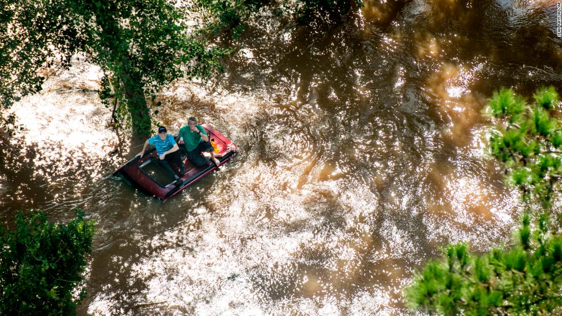 Two people near Wallace, South Carolina, sit on the top of a vehicle that was caught in flooding on Monday, September 17.