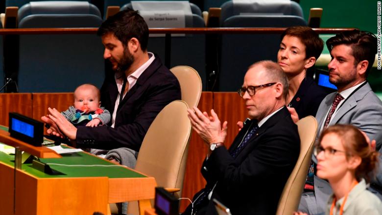 Clarke Gayford (C) claps while holding his daughter Neve, as his wife Jacinda Ardern, Prime Minister of New Zealand, speaks during the Nelson Mandela Peace Summit in the United Nations assembly hall in New York. 