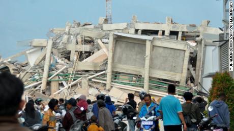Palu obyvatelé scházejí, aby pohled na zřícené budovy v důsledku zemětřesení a tsunami.
