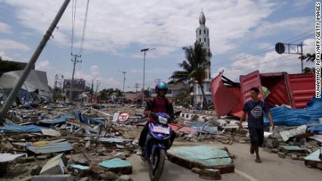 Palu lakói szeptember 29-én egy törmelékkel teli utcán haladnak. Palu körülbelül 350 000 tengerparti város.