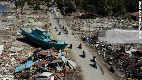Menschen fahren am 1. Oktober in Palu an einem Boot und anderen Trümmern vorbei.