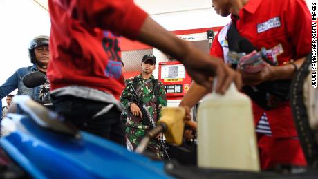 インドネシアの兵士は、10月1日にガソリン容器を満たすために人々が並ぶようにサービスステーションでガードを立っています。
