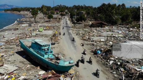 TOPSHOT - People drive past a washed up boat and collapsed buildings in Palu on October 1, 2018, after an earthquake and tsunami hit the area on September 28. - Mass graves were being readied on October 1 for hundreds of victims of the Indonesian quake and tsunami as authorities battled to stave off disease and reach desperate people still trapped under shattered buildings. (Photo by JEWEL SAMAD / AFP)        (Photo credit should read JEWEL SAMAD/AFP/Getty Images)
