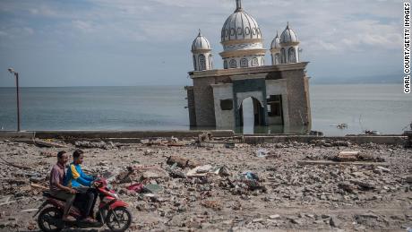 人々は2月にパルの部分的に水没したモスクを過ぎてスクーターに乗る。 モスクは地震と津波の間にその基礎からノックされました。