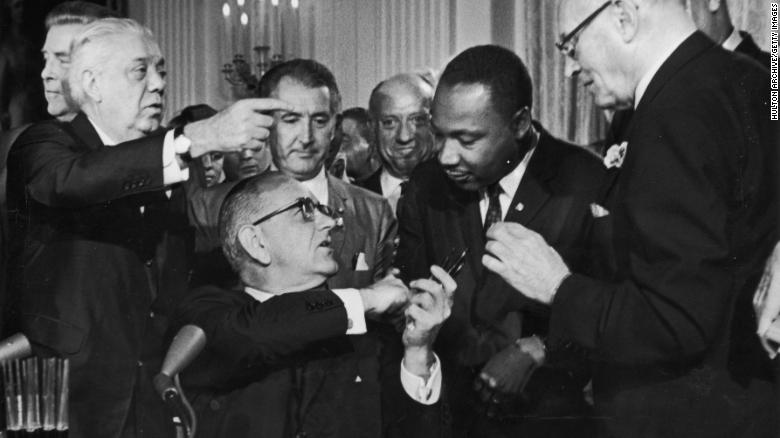 While holding multiple pens, President Lyndon Johnson greets the Rev. Martin Luther King Jr. at the signing of the 1964 Civil Rights Act. 