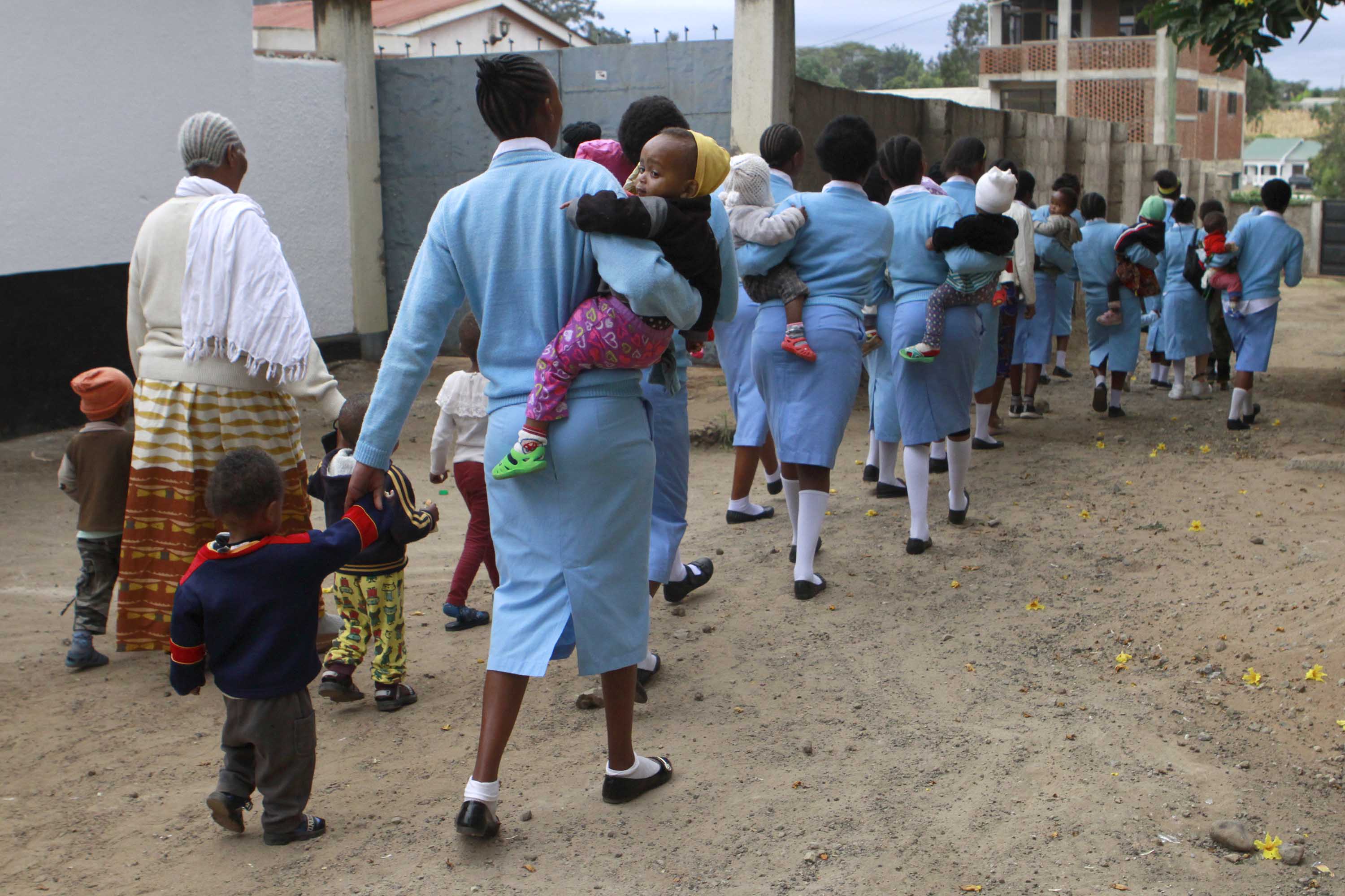 Young women dressed in uniform walk their children to daycare before attending trades courses at the Faraja Center, a shelter for vulnerable women.