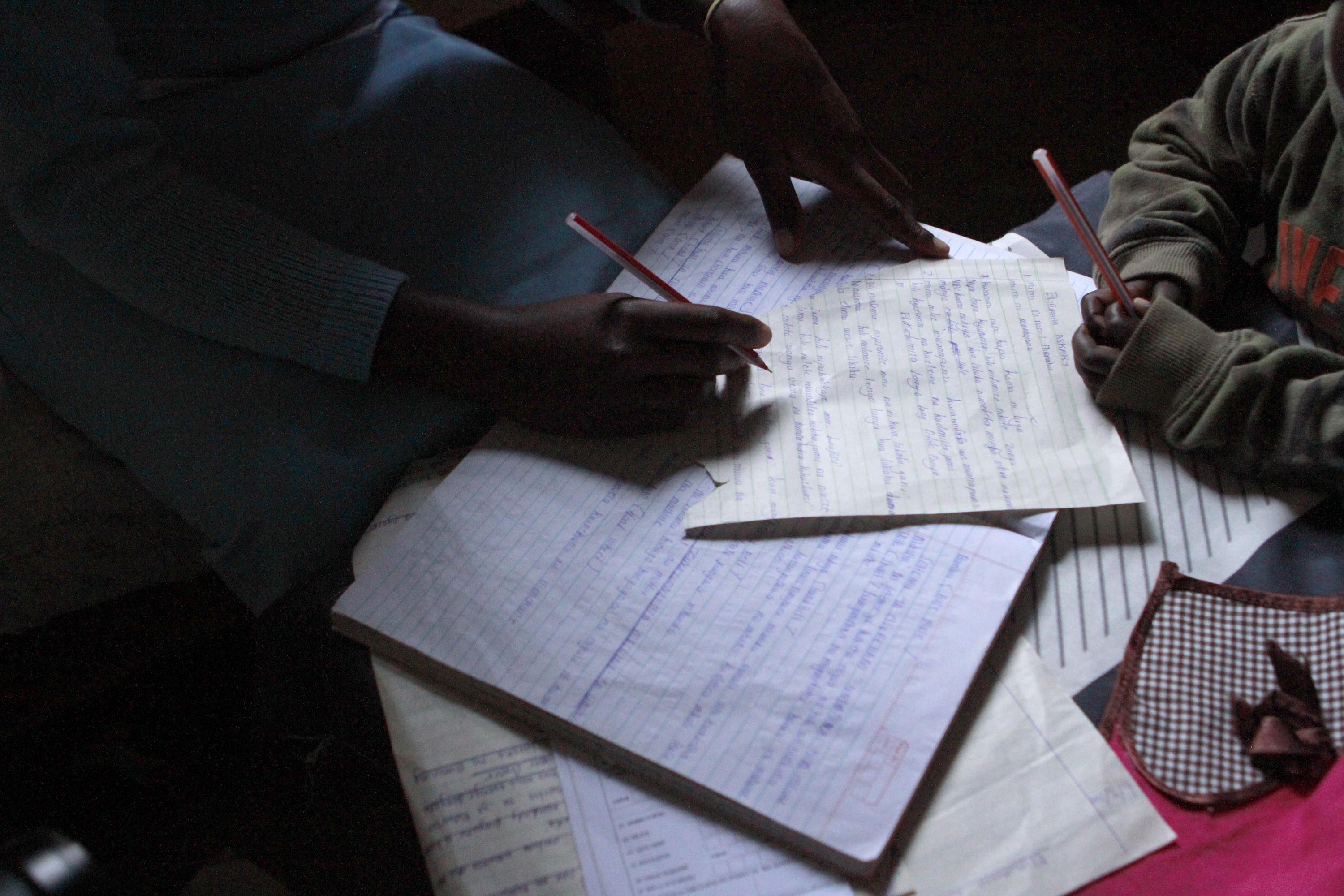 Elifuraha&#39;s son watches, pencil in hand, as she flips through her notes from a tailoring class at the Faraja Center.
