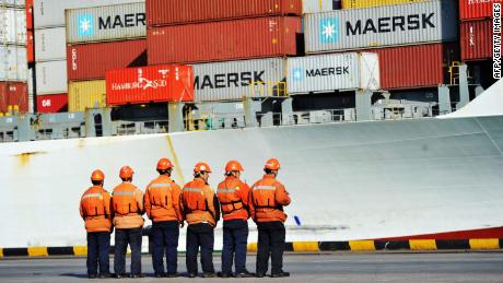 This photo taken on April 8, 2018 shows workers stand in line next to a container ship at a port in Qingdao in China&#39;s eastern Shandong province.