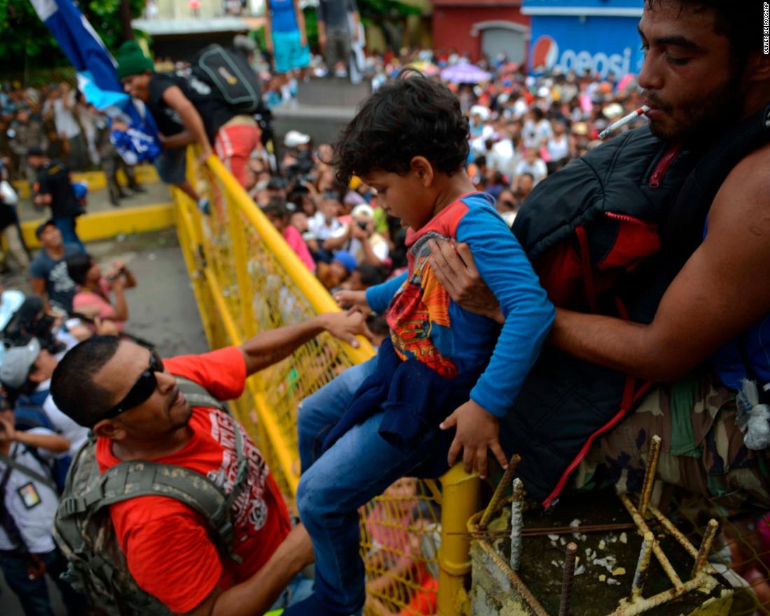 A child is lifted over the border fence as thousands of Honduran migrants rush across the border toward Mexico, in Tecun Uman, Guatemala, Friday, October 19. 