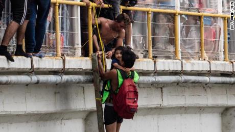 A man helps three-year-old Carlitos off the bridge and be lowered down to his mother, waiting on a raft on the river below.