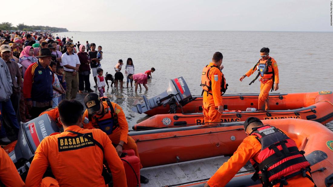 People gather on the beach as a rescue team prepares to leave the coast of Karawang.