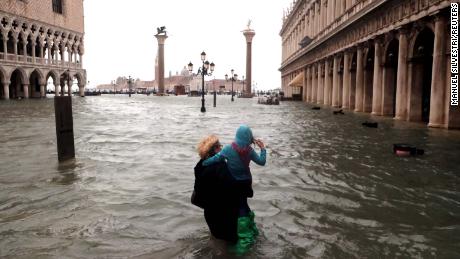 A woman holds a child as she walks in a flooded Saint Mark Square.