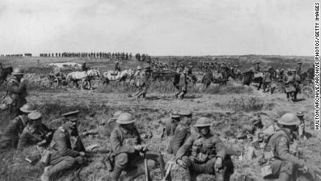 1917: Canadian troops sit and take a break in a field during a pause in their attack on the Cambrai front, France, Western Front. In the background artillery is moved by soldiers with horses.