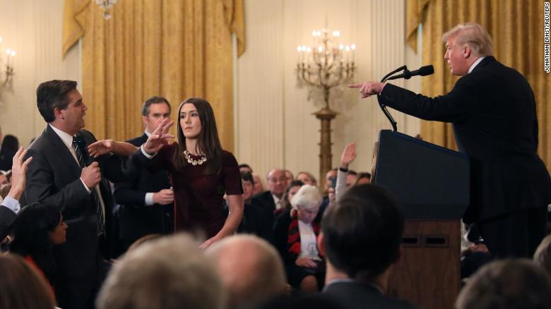 A White House staff member reaches for the microphone held by Jim Acosta as he questions Trump. 