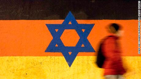A man passes by a section of the Berlin Wall with a graffiti featuring the Star of David and the Israeli flag with the German flag, by the artist  by Guenther Schaefer. East Side Gallery, Berlin.***ISRAEL OUT*** (Photo by Omer Messinger/NurPhoto via Getty Images)