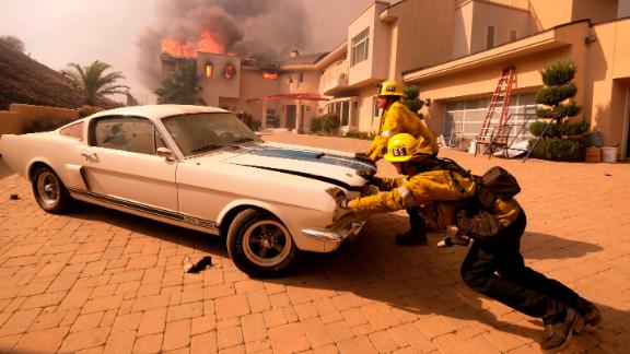 Firefighters push a vehicle from a garage as the Woolsey Fire burns a home in Malibu on November 9.