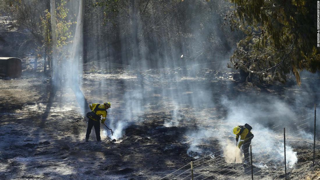 Firefighters douse embers off a canyon road that cuts across the mountains to Malibu.