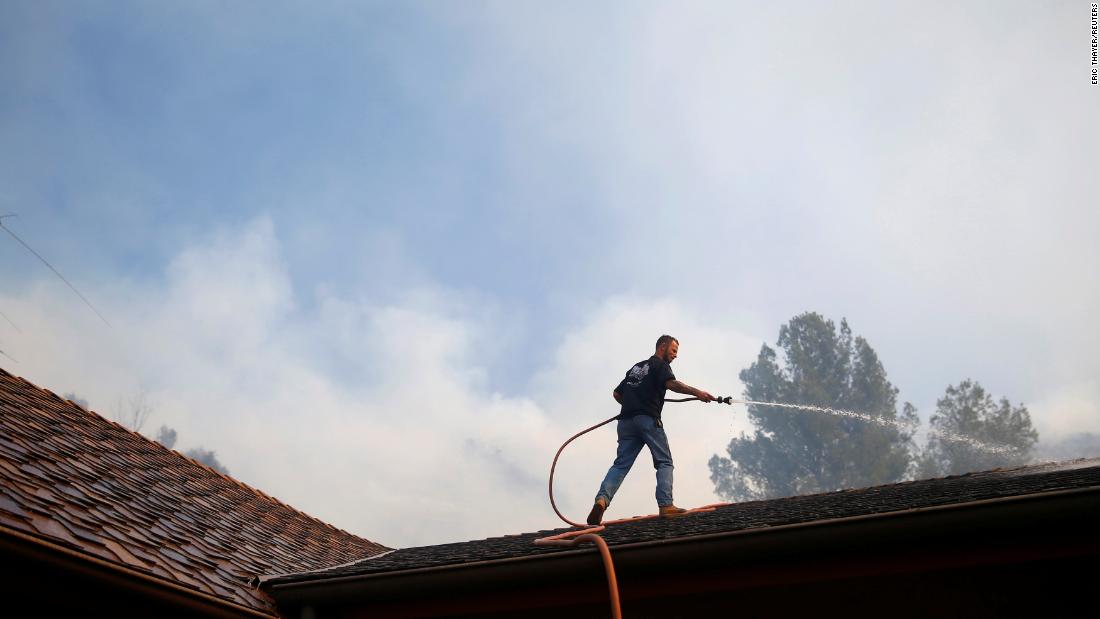 A resident sprays down a roof as firefighters battle the Peak Fire in Simi Valley.