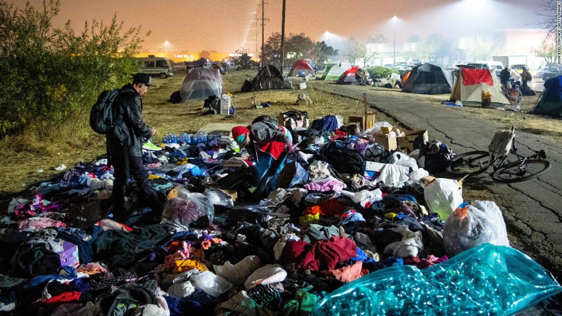 A wildfire evacuee sifts through a pile of clothing at a tent city in a Walmart parking lot in Chico, California, on Saturday, November 17.