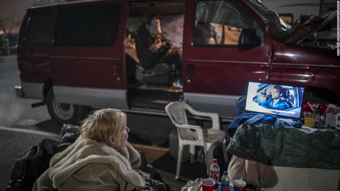 A Camp Fire evacuee watches television in the parking lot on Thursday, November 15.