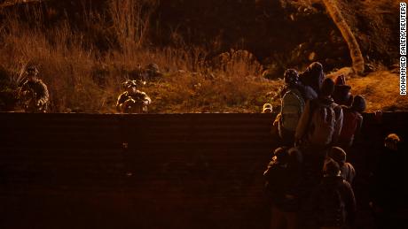 Border Patrol agents hold their guns as migrants try to go over the border fence near Tijuana, Mexico.