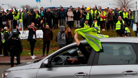 A car driver shows his yellow vest to cheer protesters as French President Emmanuel Macron visits Normandy on Tuesday.