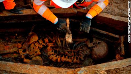An archeologist uses a brush on a skeleton in an open coffin during the excavation of the cemetery.
