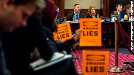 FILE-- Protesters hold up signs as Brian Huseman, left, and Holly Sullivan, executives from Amazon, testify at a City Council hearing about a deal to create a large corporate campus in New York, Jan. 30, 2019. Amazon said on Feb. 14, that it was canceling plans to build its corporate campus in New York. The deal had run into fierce opposition from local lawmakers who criticized providing subsidies to one of the world's richest companies. (Hiroko Masuike/The New York Times)