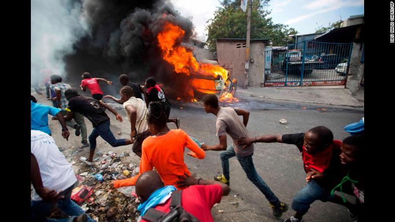 Demonstrators run away from police who are shooting in their direction, as a car burns during a protest demanding the resignation of Haitian President Jovenel Moise in Port-au-Prince, Haiti, Tuesday, Feb. 12, 2019. 