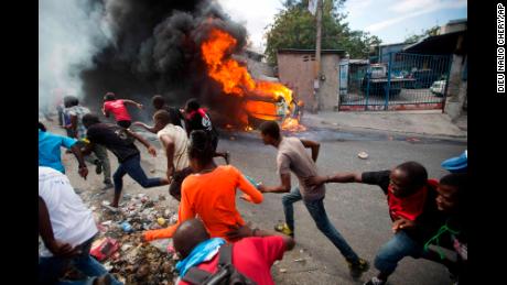 Demonstrators run away from police who are shooting in their direction, as a car burns during a protest demanding the resignation of Haitian President Jovenel Moise in Port-au-Prince, Haiti, Tuesday, Feb. 12, 2019. 