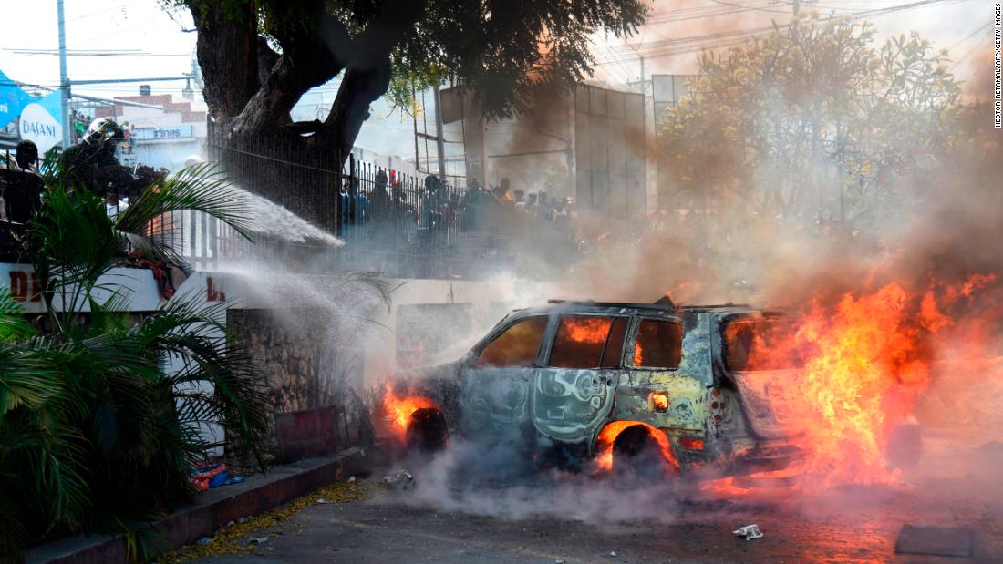 Firefighters extinguish burning cars at the offices of Haiti&#39;s state television station on February 13.