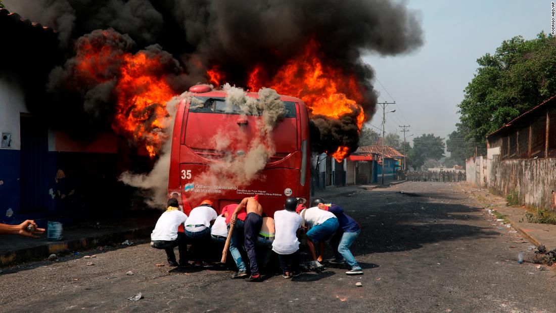 Demonstrators push a bus that was set on fire during clashes with the Venezuelan National Guard in Urena, Venezuela, on February 23.