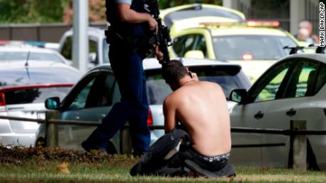 A man rests on the ground as he speaks on his mobile phone across the road from mosque in central Christchurch, New Zealand, Friday, March 15, 2019. A witness says a number of people have been killed in a mass shooting at a mosque in the New Zealand city of Christchurch; police urge people to stay indoors. (AP Photo/Mark Baker)