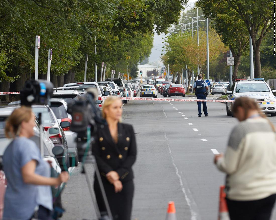 Members of the media wait around the scene as police officers cordon off the area.